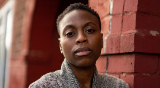 Portrait of a woman against a brick wall, holding her arm protectively