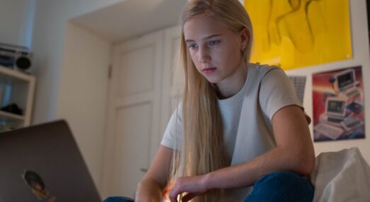Teenage girl sat on her bed looking at her laptop