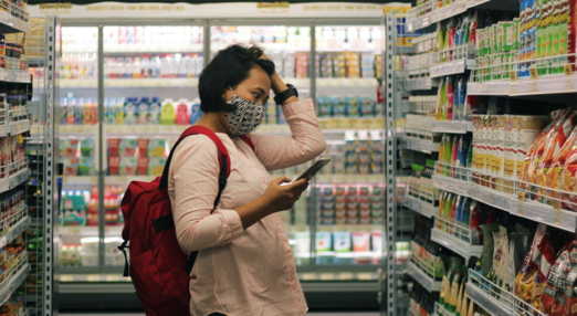 A woman in a supermarket looks at produce while holding her head